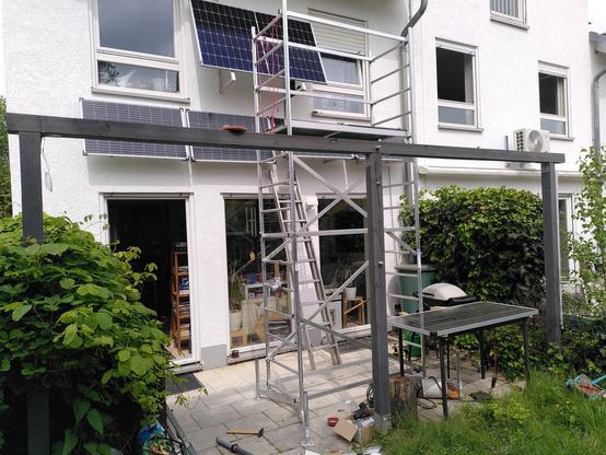 Ein Gerüst, eine Hausfassade mit 5 PV-Modulen, sehr viel Unordnung auf der Terrasse davor.