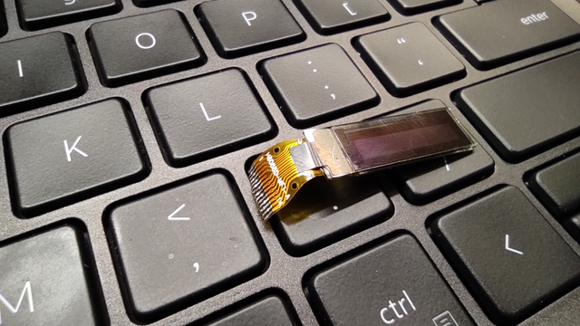 The OLED display on a ribbon cable lying on the laptop keyboard.
