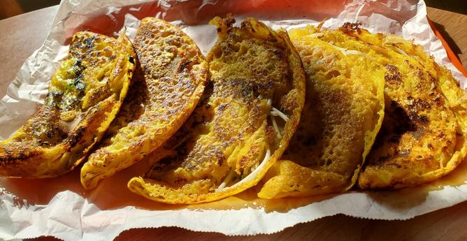 Tray of 5 Vietnamese savoury banh xeo (Vietnamese crepes) on a plastic orange cafeteria tray, atop the wax paper.