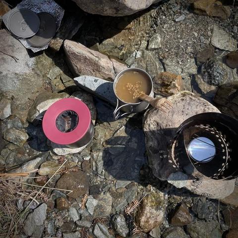 Cup of lentil soup, and mug with a reusable coffee filter  and coffee in, stove windshield.