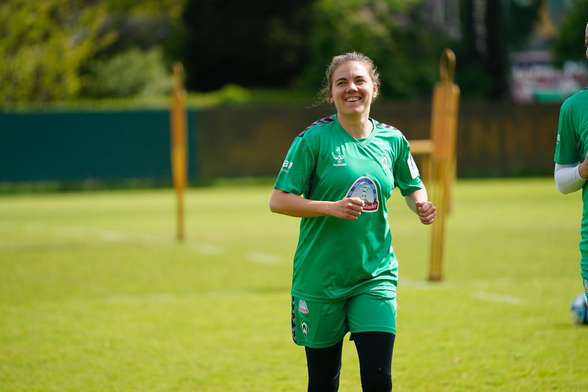Ein Foto von Rieke Dieckmann auf dem Trainingsplatz. Sie joggt in grüner Trainingskleidung und lächelt an der Kamera vorbei.