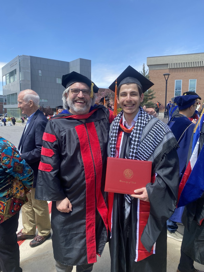 A professor next to his student in cap and gown on graduation day