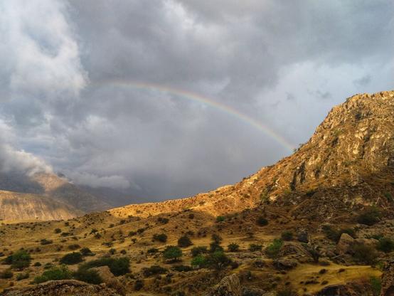 تصویری از کوهستان. شامل کوه‌ها، آسمان ابری و رنگین کمان .