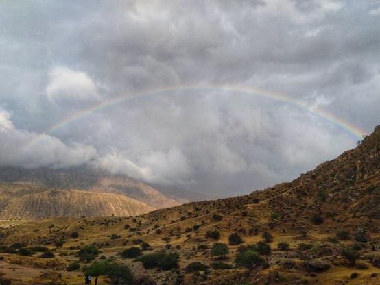 تصویری از کوهستان. شامل کوه‌ها، آسمان ابری و رنگین کمان .