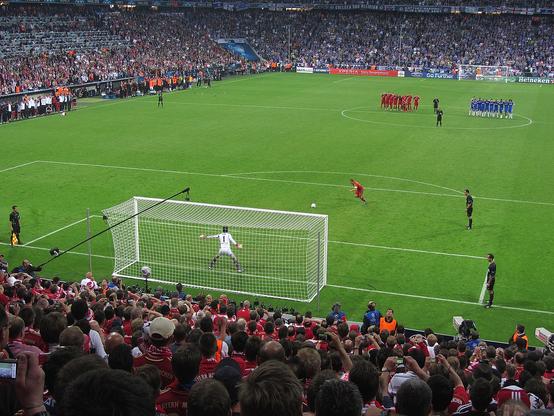 Philipp Lahm schießt einen Elfmeter im Champions-League-Finale der Männer zwischen dem FC Bayern München in roten Trikots und dem FC Chelsea in blauen Trikots. Das Foto wurde von der Tribüne aus aufgenommen, vor der sich das Tor befindet, auf das der Elfmeter geschossen wurde.