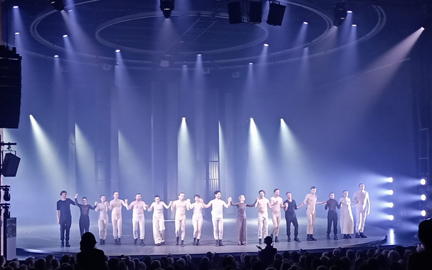 Die Bühne ist von feinem Nebel erfüllt. Das ganze Ensemble verbeugt sich (4 schwarz gekleidete Musiker:innen und die Schauspieler:innen).
Fast alle sind in weiß gekleidet, die Darstellerin des Nathan in grau.
Die Bühne wird von oben und von der Seite beleuchtet, durch den Nebel sieht man die Lichtkegel der Scheinwerfer.