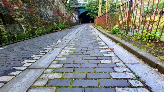 A stone tramway leading down a steep cobbled street towards a Victorian cast-iron bridge.
