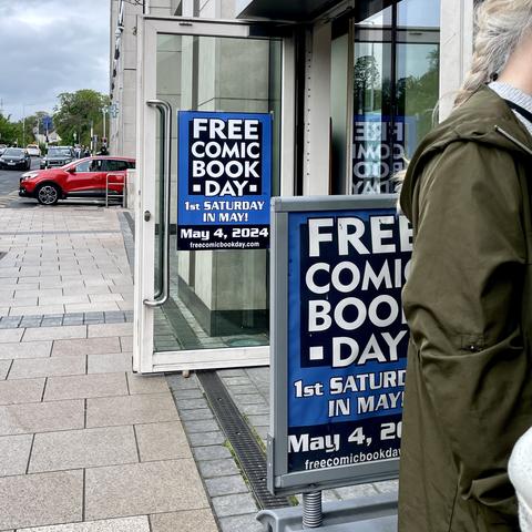 Outside Big Bang Comics Shop Dundrum. Promotional signs for "Free Comic Book Day" on May 4, 2024, with a top of queue partially visible on the right.