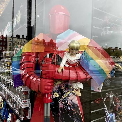 Forbidden Planet shop window display with collectible items including life size red Imperial Guard figure and smaller doll in his arms, overlaid with the a rainbow flag.
