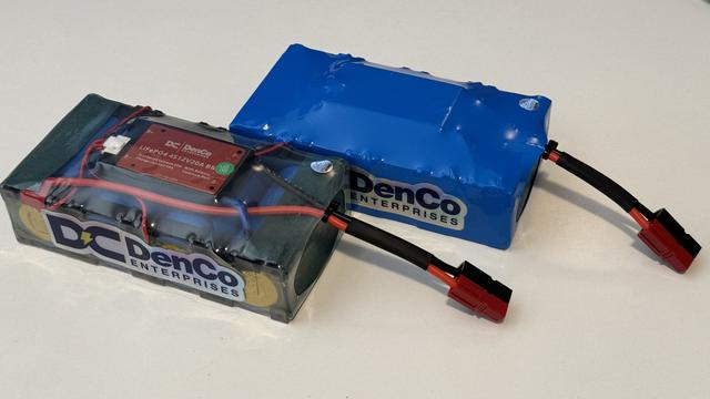 A clear wrapped DenCo 5.5Ah LiFePO4 battery next to a standard DenCo 5.5Ah flat pack battery.