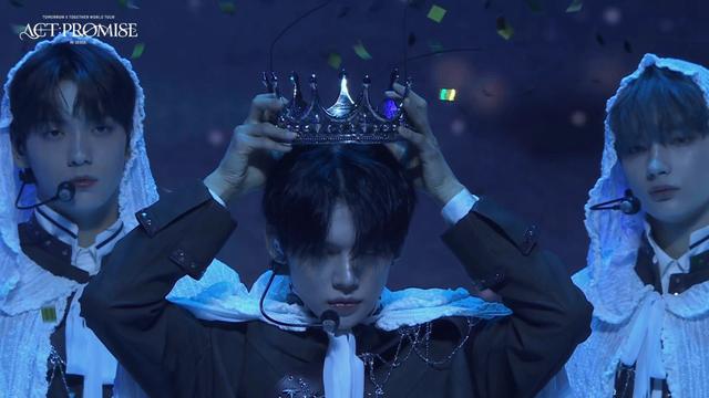 Yeonjun putting on his crown while Soobin and Kai watch from behind