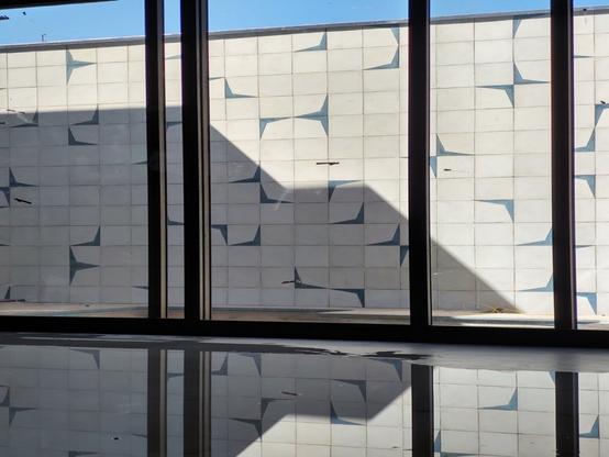 Parede de ladrilhos hidráulicos no fundo, uma porta de alumínio de correr e um piso molhado refletindo tudo