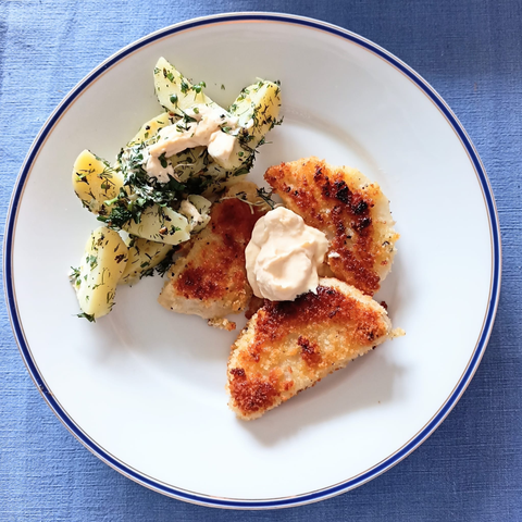 drei Selleriestücke kross gebraten auf einem Teller, dazwischen ein Klacks Mayonnaise. Daneben einige Kartoffelspalten mit Kräutern und etwas Mayonnaise