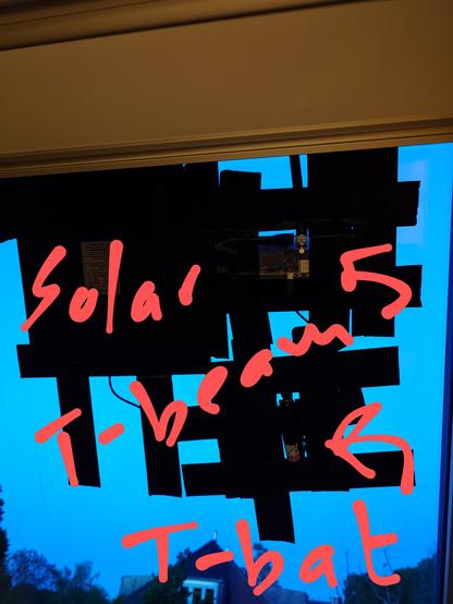 Solar pannel T-bat and T-beam stuck with duct tape on inside of roof window with words written to label. The dusk blue sky is in the background.