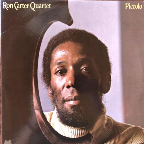 Cover of record album showing Ron Carter looking through cut out of piccolo bass. Text on cover says, “Ron Carter Quartet” and “Piccolo.”