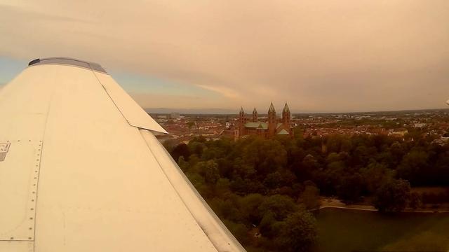 Blick aus dem Fenster eines Kleinflugzeugs im Quearanflug auf Piste 16 von Speyer (EDRY): der Dom, Teile vom Stadtzentrum, Wald, und die Hinterkante der Tragfläche mit ausgefahrenen Landeklappen sind zu sehen.