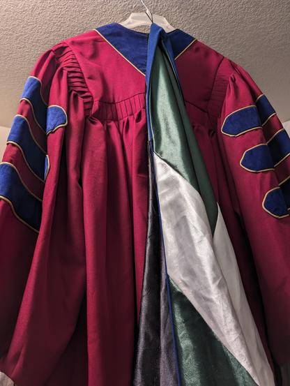 Regalia in red with blue chevrons and a green and white doctoral hood.