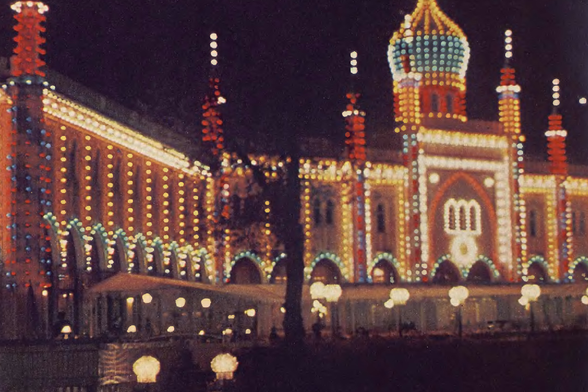 1956 Festive Night Scene at the Circus-Palace

The image captures a vibrant night scene at a carnival or circus building.
The building is lit up with numerous bright lights and features architectural details such as a dome and arched windows adorned with decorative lights.
It is situated in what appears to be an urban setting, as evidenced by the presence of street lamps and buildings in the background.
There is a sense of celebration or event, given the festive lighting and the decorations, which might include flags or banners.
The image does not contain any text.