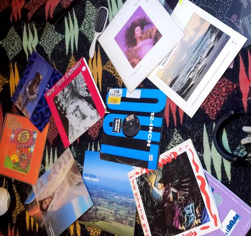 A blanket with a bunch of vinyl records on it that were played in the mix. Also visible are some headphones and an empty bowl and spoon.