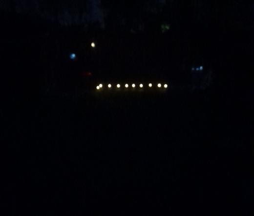 Dark night, solar lights lit up. A string of 10 white lights along the ground. 4 lights on thr fence, blue red white