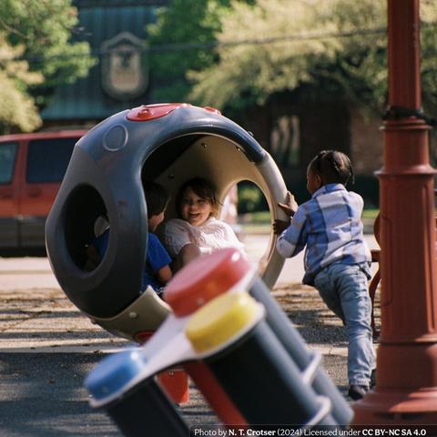 Color photograph of three children playing with a piece if playground equipment all children instinctively call a "space ball" for some reason.