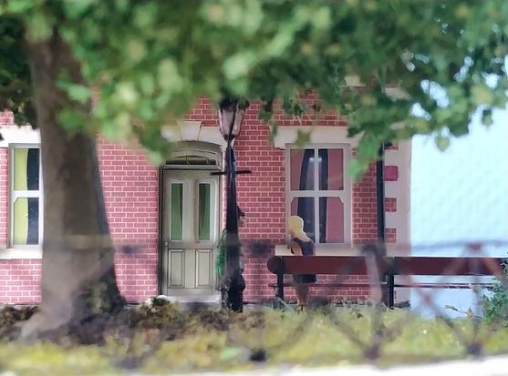 Detail of a model railway showing the brick facade of a house behind a park with a large chestnut tree. ¦ Detail van een modelspoorbaan met zicht op een bakstenen façade van een woonhuis achter een park met een grote kastanjeboom.