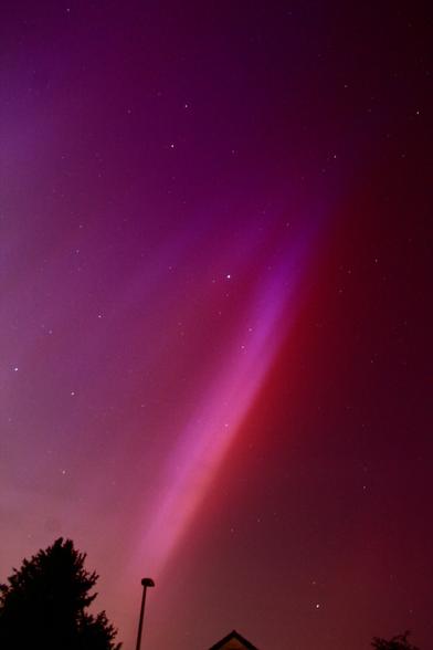 Red/Purple Aurora Borealis over silhouetted tops of a house and a street lamp.