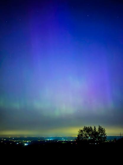 A night sky with aurora lights above a silhouetted landscape with city lights.