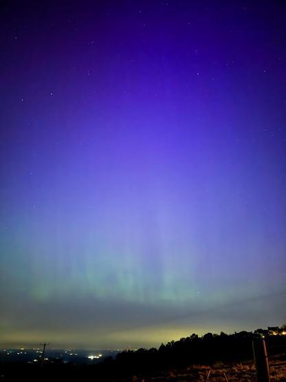 Night sky with stars and faint aurora lights over a silhouetted landscape.