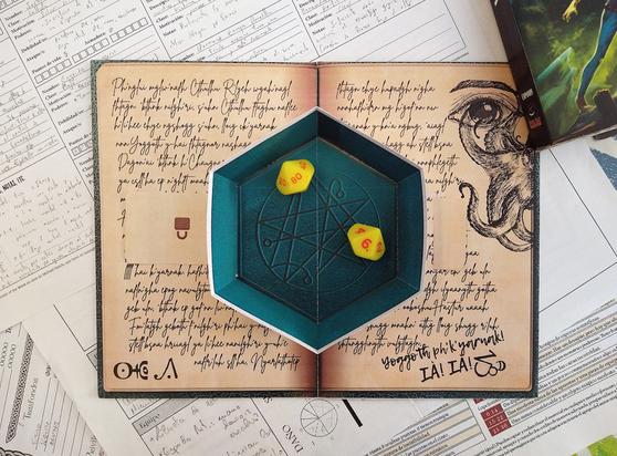 Foto centrada de la bandeja lanzadados "Cthulhu", que parece un cuenco aterciopelado verde sobre un diario lovecraftiano manchado de sangre.