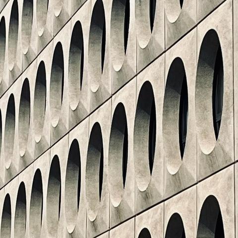 Close-up of a building facade featuring a pattern of arched openings in concrete, creating a rhythmic and textured visual effect.