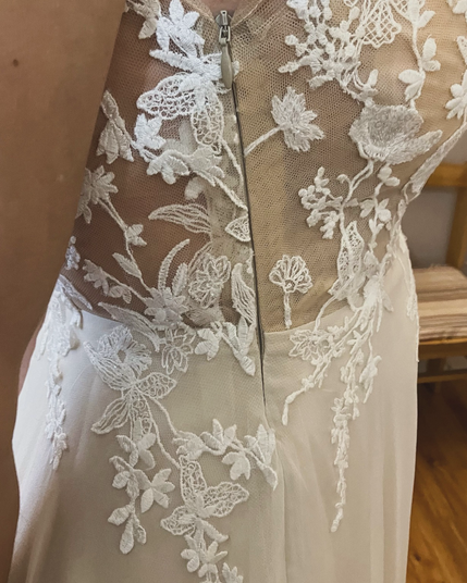 Profile view of the bodice of a wedding dress made from illusion mesh embellished with ivory lace. The side seam has been sewn with an invisible zipper .