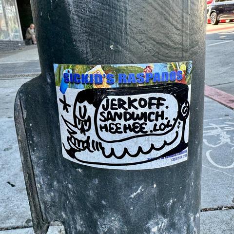A slap sticker spotted on the street. A drawing of a man's face, he has a pointy nose and a goatee and a mischievous expression. "Jerkoff. Sandwich. Heehee. LOL." is written near his head.  The art is drawn in sharpie on a sticker label that is mostly white, but has "Sickid's Raspados" printed on the top.