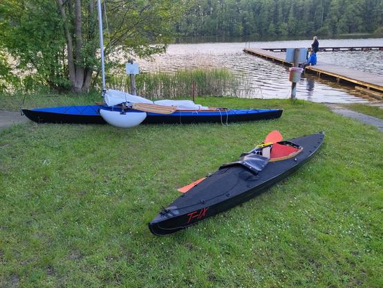 A klepper T9 in the front and a two seater folding kayak behind it both are on the shore of a lake.