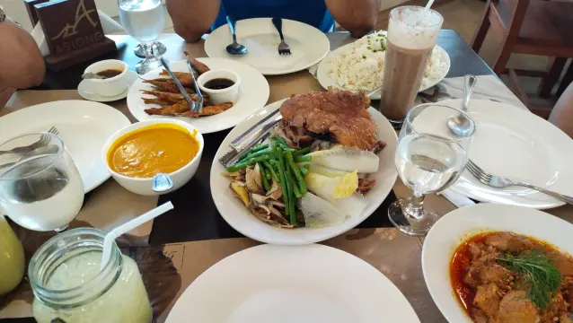 Meals served in Asiong Caviteño Restaurant. Includes crispy tawilis, crispy pata (with karekare sauce separate on side), adobong pula, and a platter of garlic rice. Drinks like cold chocolate and in-house basil cucumber lemonade are also shown