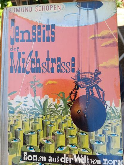 Cover des Romans "Jenseits der Milchstraße" von Edmund Schopen. Ein kugelförmig Apparat wird aus einem UFO abgesenkt. Am Boden ein Wald aus Bambusgewächsen, die oben mit Augäpfeln versehen sind.