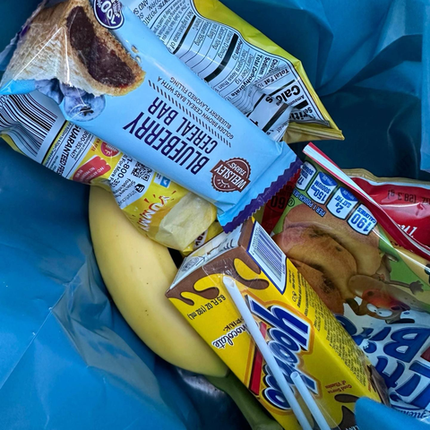 An assortment of snacks in a bag: yoo-hoo, cereal bars, chips, and mini muffins