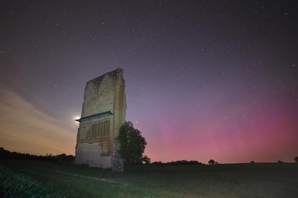 a few pink aurora beams and moon just hiding behind the ruin