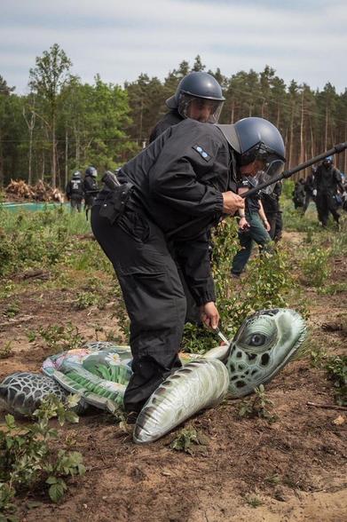 Ein Polizist steht über einer großen aufblasbaren Sumpfschildkröte und sticht ihr mit einem Messer ins Genick. Im Hintergrund weitere Cops und eine Wald.