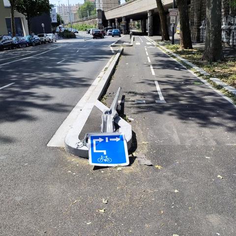 Début d'une voie cyclable avec un panneau bleu et pylône à terre, enfoncés par une voiture très sûrement...
