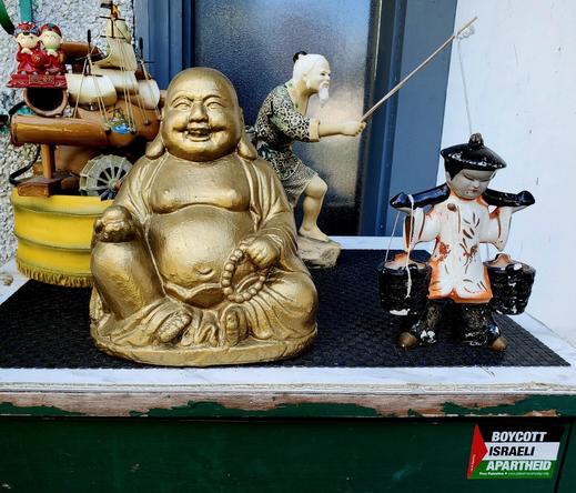 Our front porch table with golden small Buddha, water carrier figurine, fisherman with pole figurine, mini waterfall piece with Chinese figurines & a BOYCOTT ISRAEL APARTHEID sticker