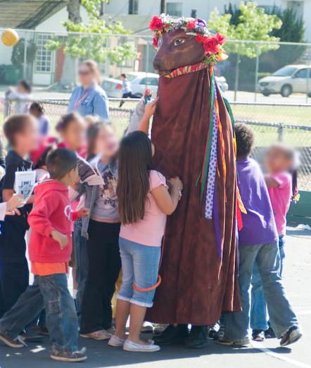 Lucy the Bear being mobbed by children in a playground. The children's faces are blurred.