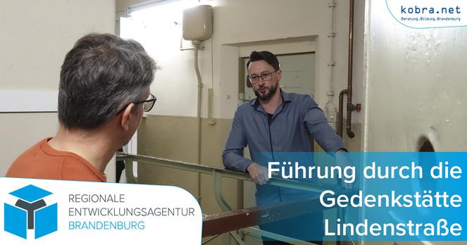 Ein auf dem Flur stehender Gedenkstättenmitarbeiter erklärt einem in einer Zellentür stehenden Gast auf dem Flur der Gedenkstätte dieselbe.