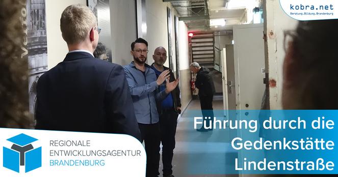 Ein Gedenkstättenmitarbeiter erklärt mehreren Gäst*innen auf dem Flur der Gedenkstätte dieselbe.