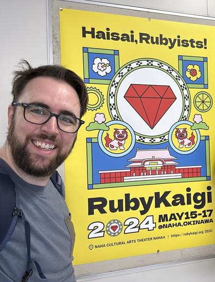 Photo of tired traveler in front of ruby kaigi 2024 poster