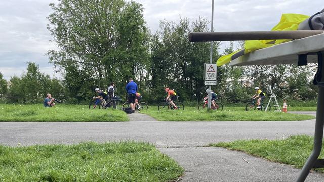A line of 5 racing cyclists on a track crossing the picture right to left