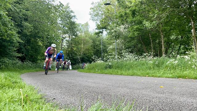 A racing cyclist turning a corner on a circuit surrounded by trees with a number of others in the background.