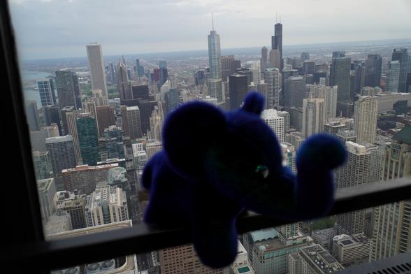 Slonik perched atop a skyscraper with the Chicago skyline behind
