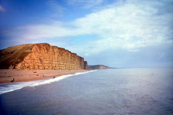 A distinctive, sand-coloured cliff, overlooking a beach.