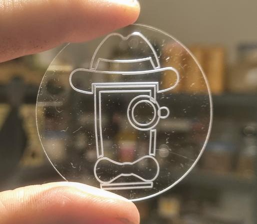 A clear acrylic disc held between a thumb and an index finger - a sort of pint-guy-inna-hat with a bowtie and monocle logo engraved on it.